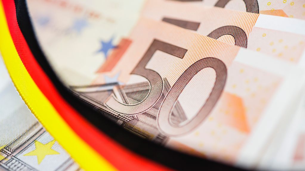 Zu sehen sind gefächerte 50-Euro-Scheine und eine schwarz-rot-goldene Banderole.