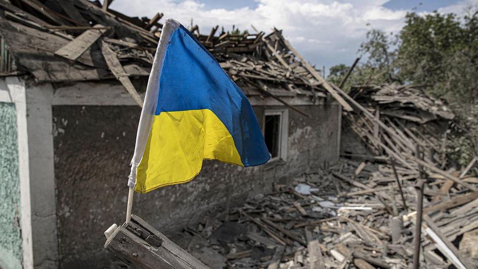 Die ukrainische Fahne weht über einem vom Krieg zerstörten Haus.