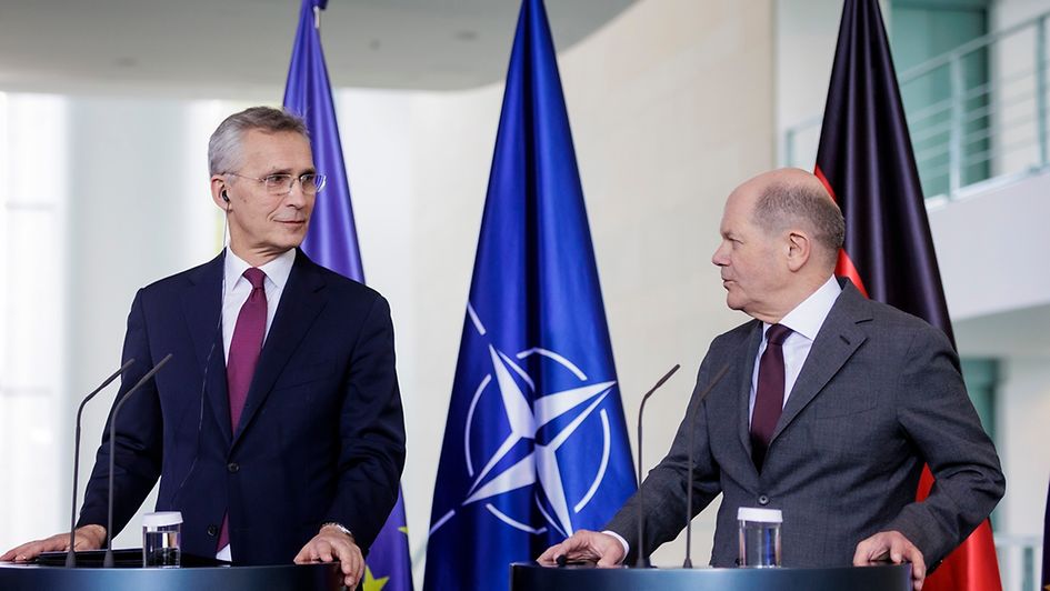 NATO-Generalsekretär Stoltenberg (l.) steht mit Kanzler Scholz an den Redepulten während der Pressekonferenz. Im Hintergrund stehen drei Flagge: EU, NATO und Deutschland.