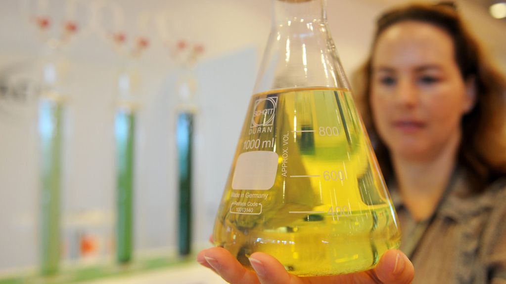 Frau in Labor hält Gefäß mit gelber Flüssigkeit.