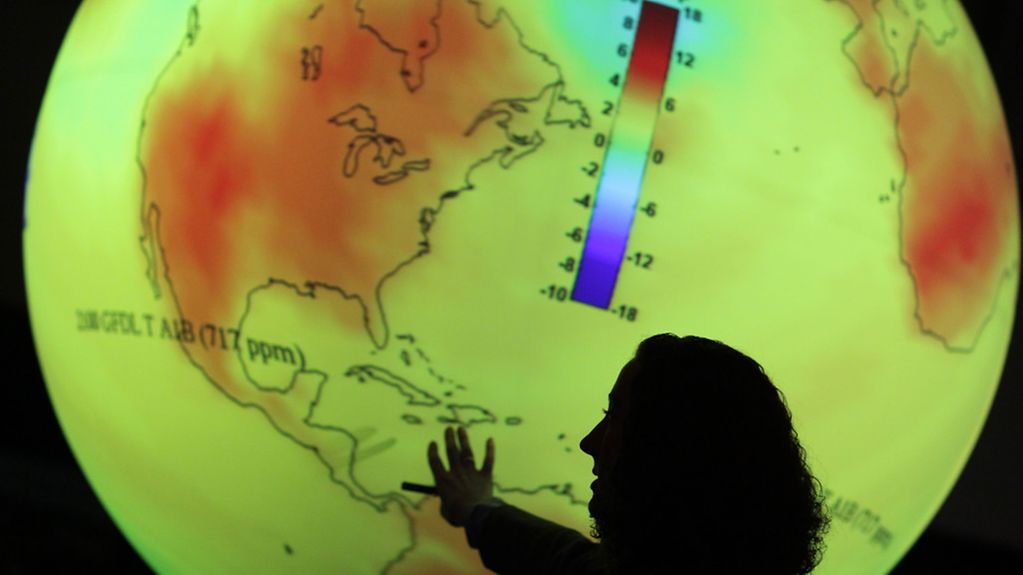 A woman at a lit-up globe explains climate change.