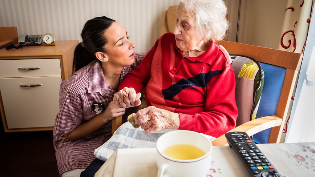 Pflegefachkraft in Senioren- und Pflegezentrum mit einer Seniorin am Tisch