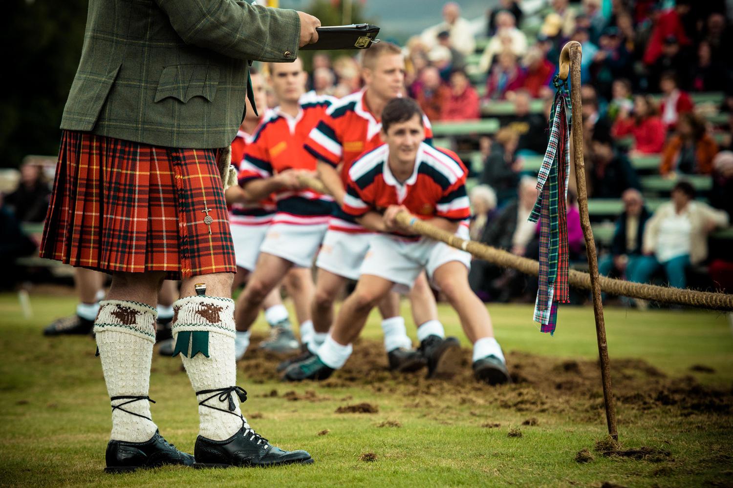 Ein Team steht am Start im Tauziehen-Wettbewerb, im Vordergrund ein Kampfrichter im Kilt. Braemar, Scotland