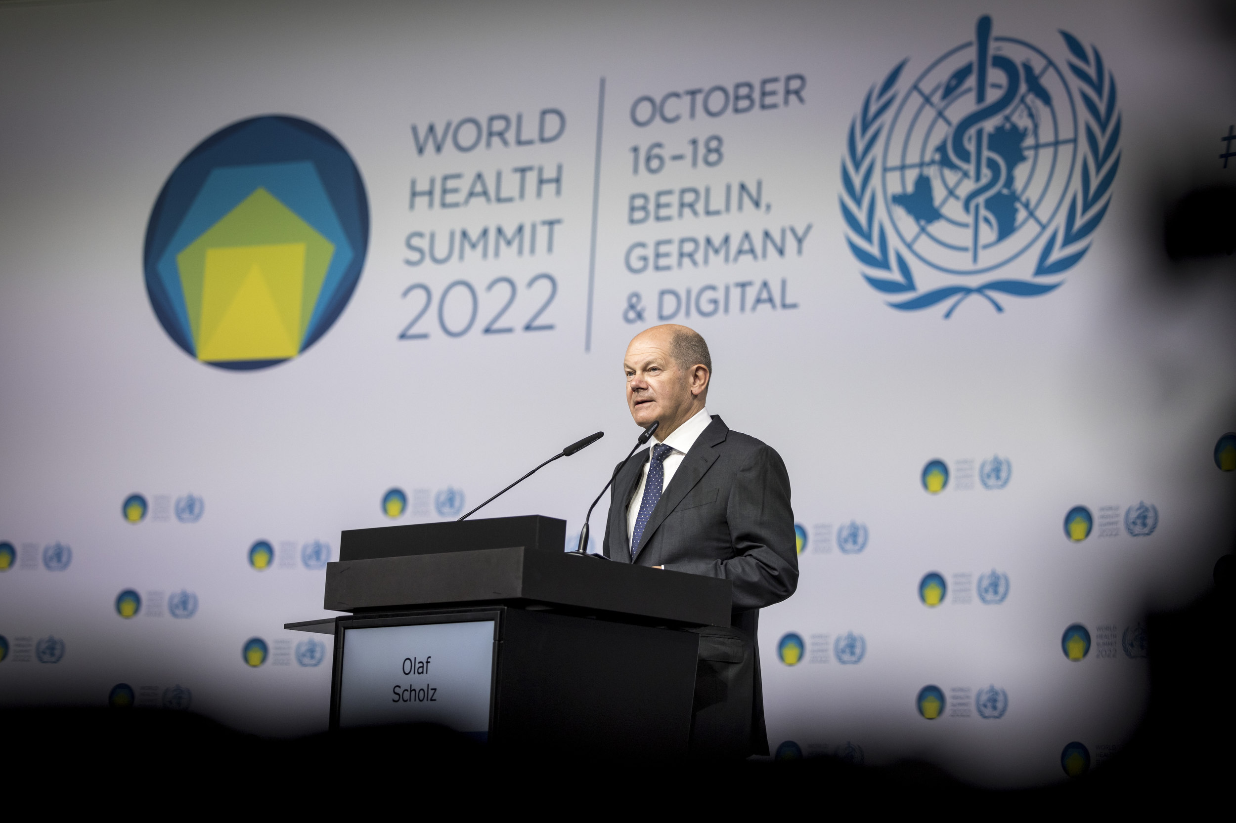 Auf dem Bild ist Bundeskanzler Olaf Scholz hinter einem Rednerpult auf dem World Health Summit zu sehen. 