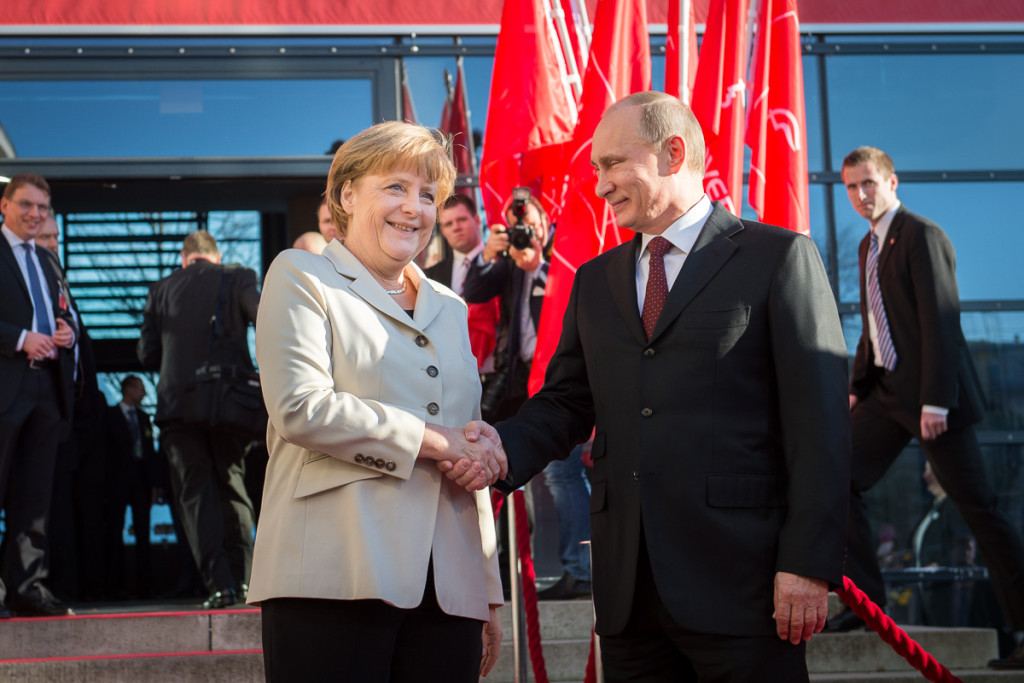 Merkel begrüßt Putin vor Messefahnen.