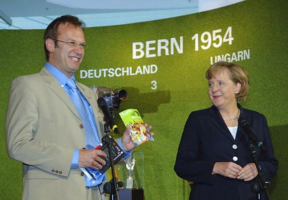 La chancelière fédérale, Angela Merkel, et le directeur de la KOS, Thomas Schneider, présentent le Fanguide de la Coupe du monde de football à l'exposition sur le Mondial à la Chancellerie fédérale.
