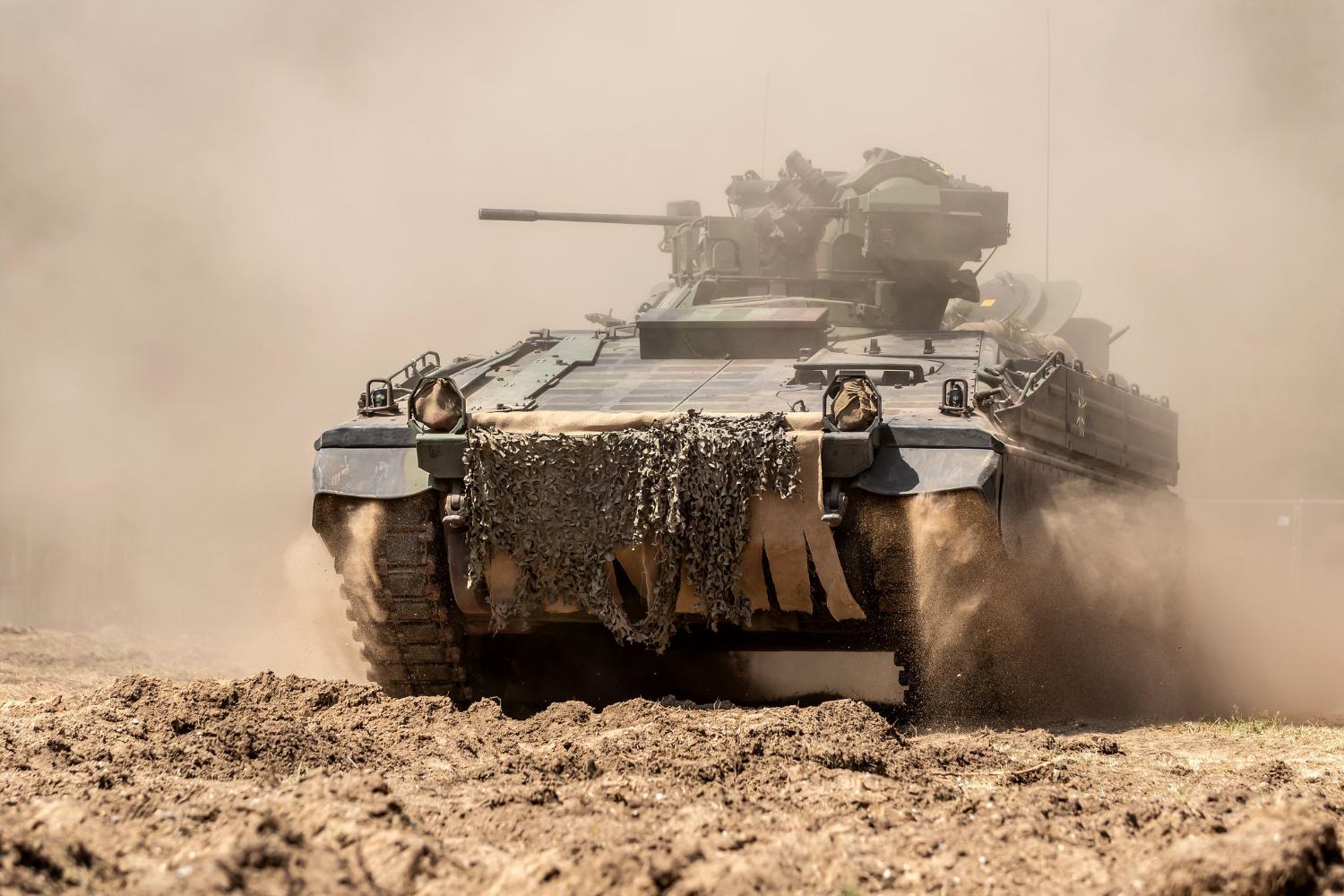 Ein Panzer fährt über eine staubige Straße.