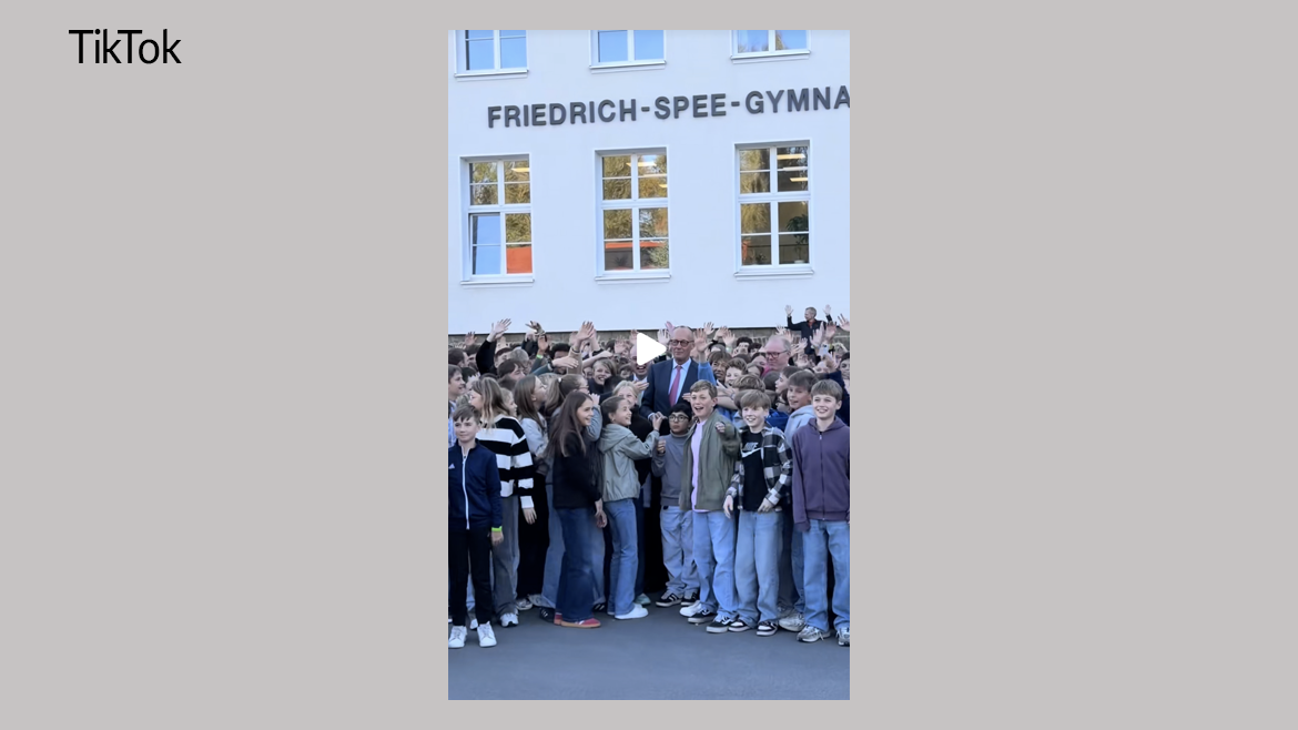 Bundeskanzler Merz mitten in einer Gruppe von Schülerinnen und Schülern vor dem Friedrich-Spee-Gymnasium.