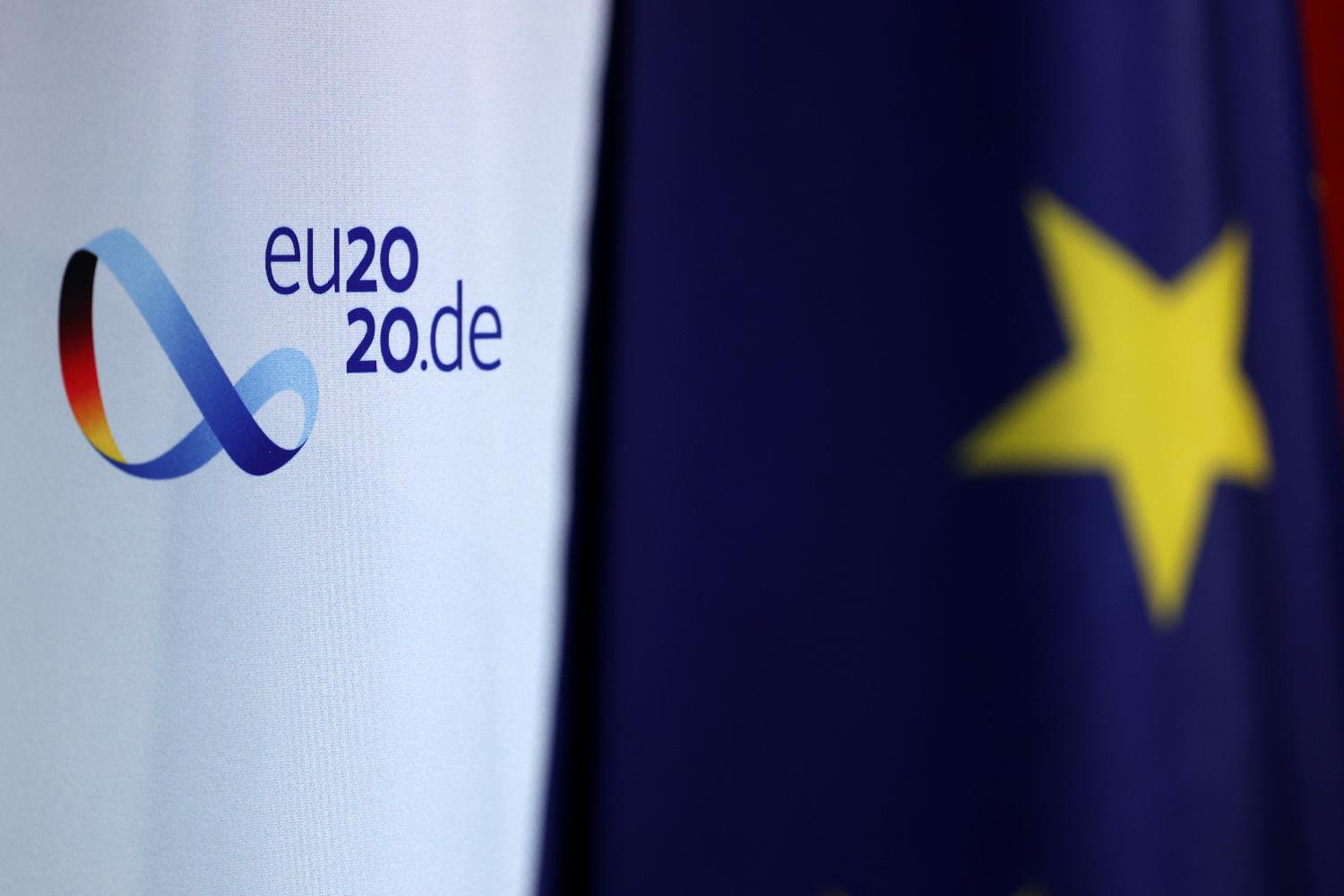 Logo der deutschen EU-Ratspräsidentschaft und Europa-Fahne im Vordergrund.