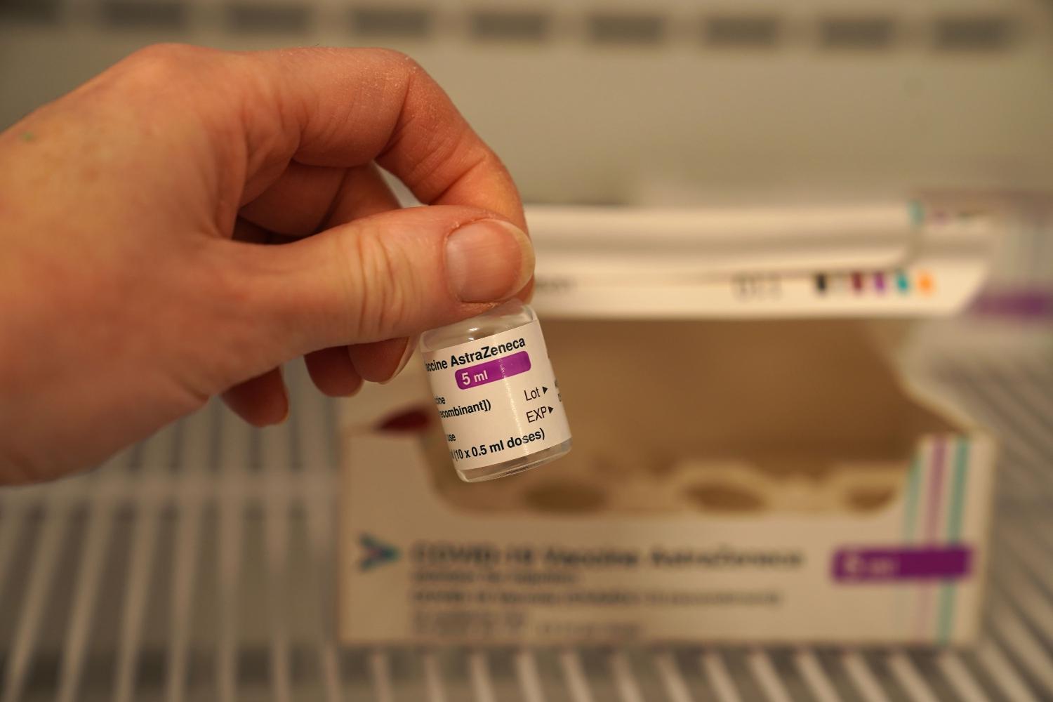 Das Bild zeigt eine Hand, die ein Fläschchen mit der Aufschrift AstraZeneca aus einem Kühlschrank nimmt.