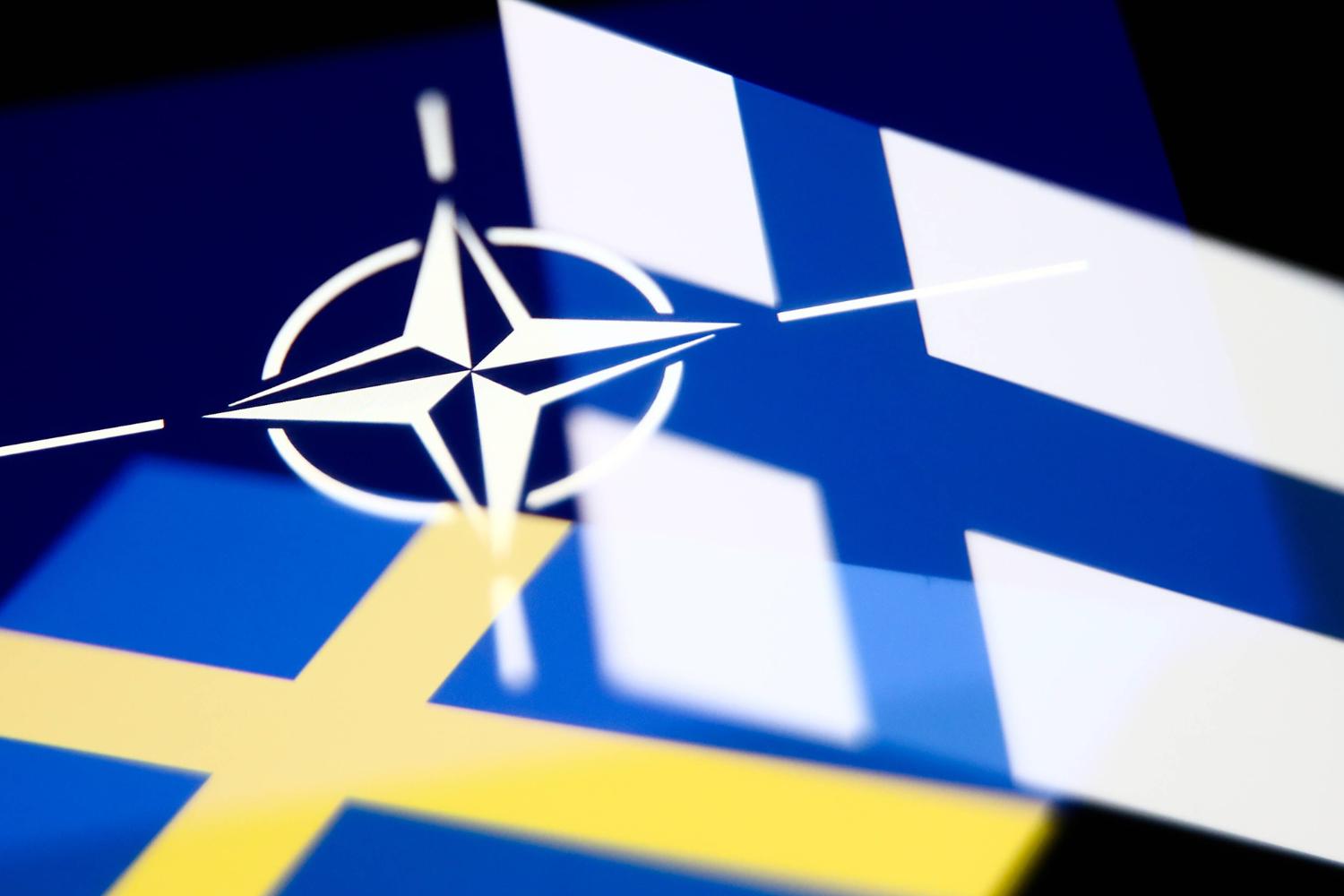 The photo shows the Finnish and Swedish flags and the NATO logo