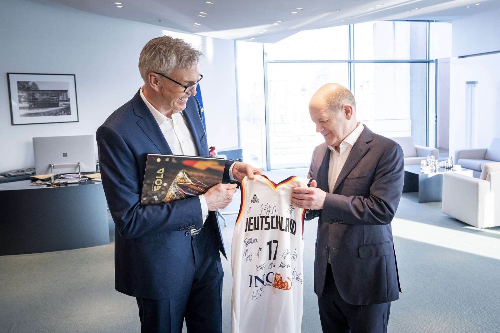 Basketball-Nationaltrainer Gordon Herbert (l.) überreicht Bundeskanzler Scholz ein unterschriebenes Basketball-Trikot.