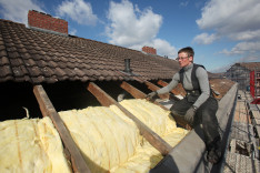 Eine Dachdeckerin verlegt Mineralwolle zur Wärmedämmung auf einem Dach