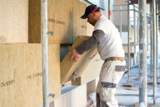 Ein Mitarbeiter setzt auf einer Baustelle zur Dämmung der Fassade eine Steinwollplatte an einer Hauswand an. Foto: Klaus-Dietma
