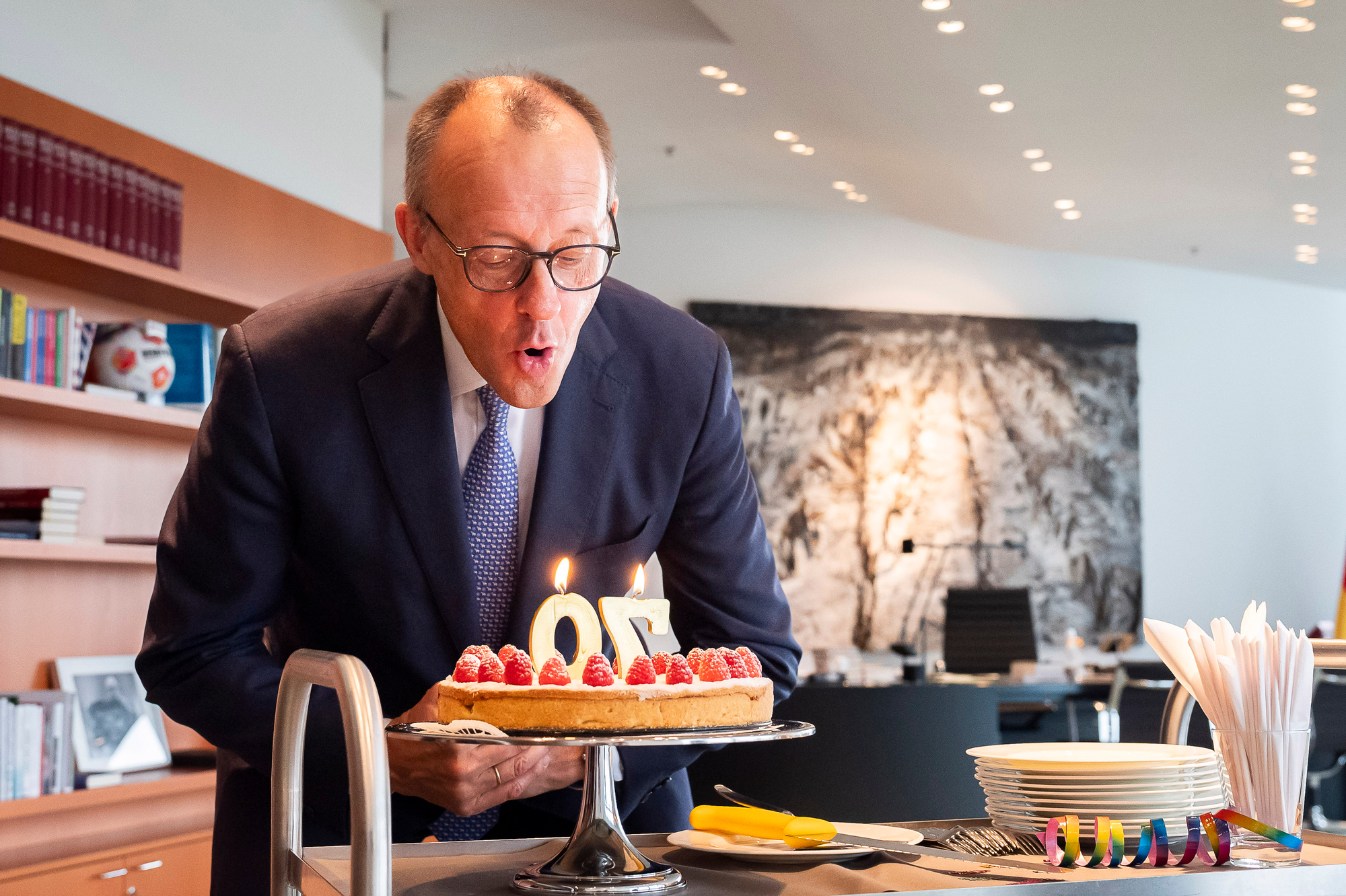 Das Foto zeigt Bundeskanzler Friedrich Merz beim Ausblasen von Geburtstagskerzen auf einem Kuchen.