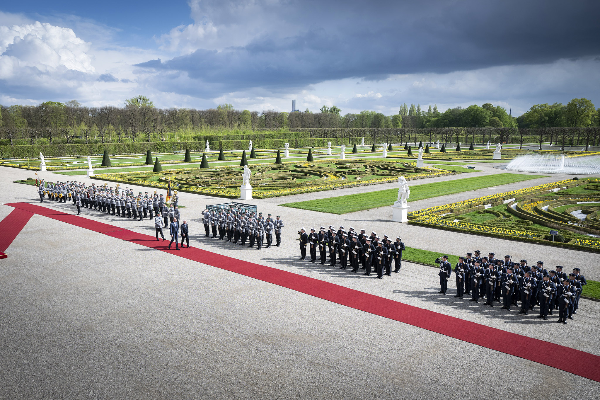 Der Bundeskanzler und der brasilianische Präsident inspizieren auf einem roten Teppich die Ehrenwache der Bundeswehr. Im Hintergrund der Schlossgarten von Schloss Herrenhausen.