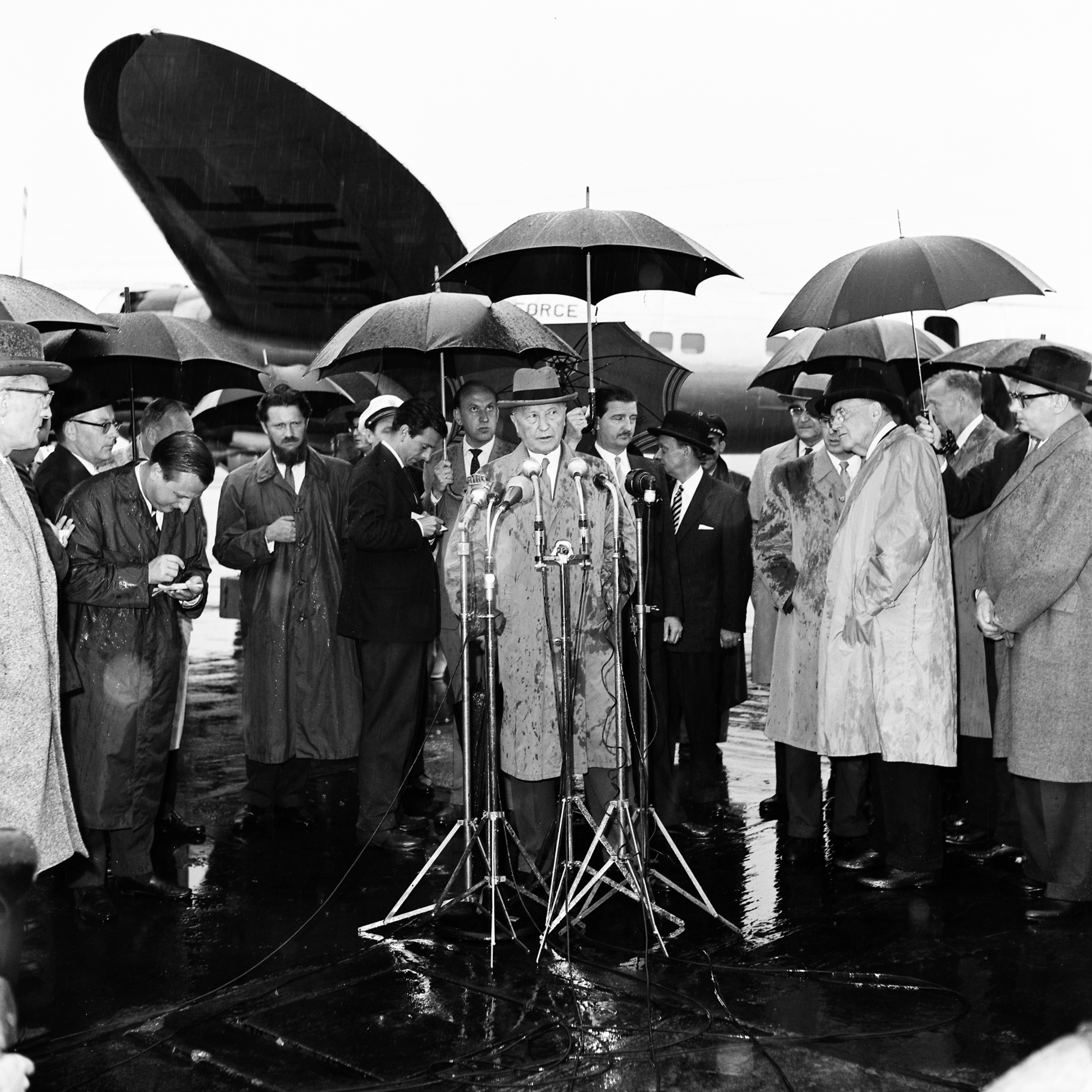Schwarz-weiß-Fotografie aus dem Jahr 1958 zeigt Bundeskanzler Konrad Adenauer (am Mikrofon) während eines Pressestatements auf dem Flughafen Köln-Wahn.