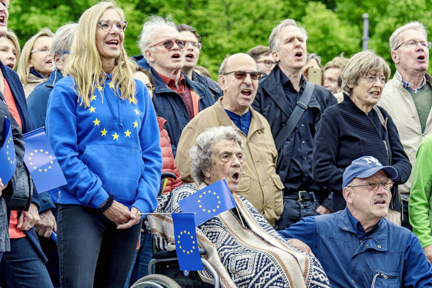 People of all ages with European flags and logos sing together.
