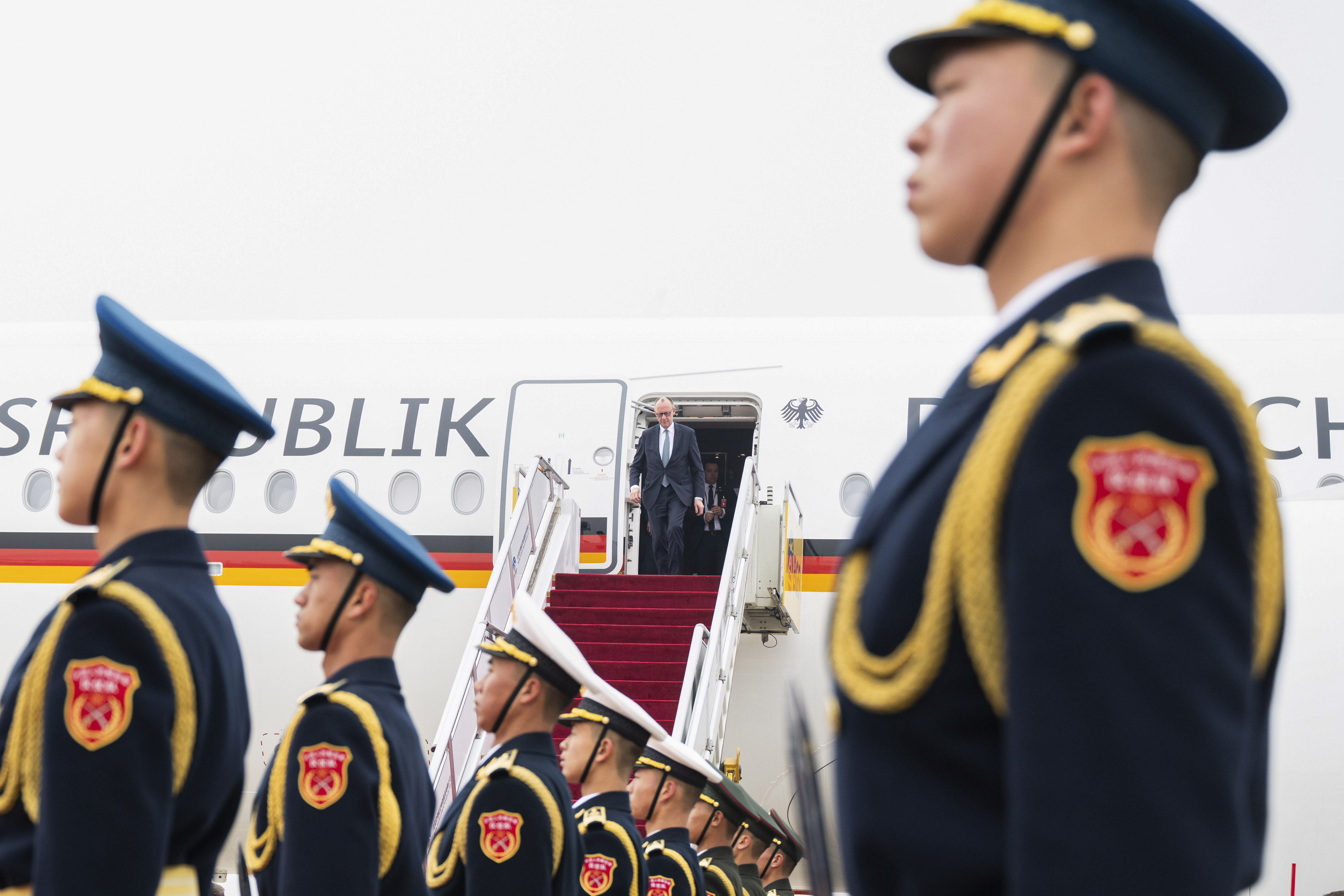 Le chancelier fédéral Merz descendant de l’avion gouvernemental ; au premier plan, une garde d’honneur chinoise.