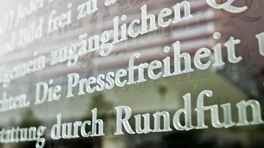 Das Wort Pressefreiheit als Ausschnitt des Grundgesetzartikels 5 auf einer Glasscheibe.