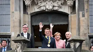 Chancellor Angela Merkel and French President Emmanuel Macron wave from the balcony of the town hall.