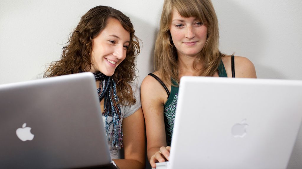 Zwei junge Frauen sitzen auf dem Fußboden mit Laptops auf den Knien