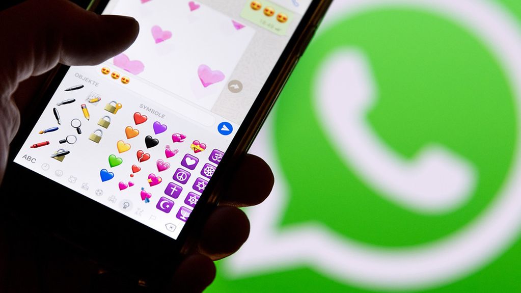Ein Smartphone mit Emojis aus WhatsApp vor dem WhatsApp-Logo.