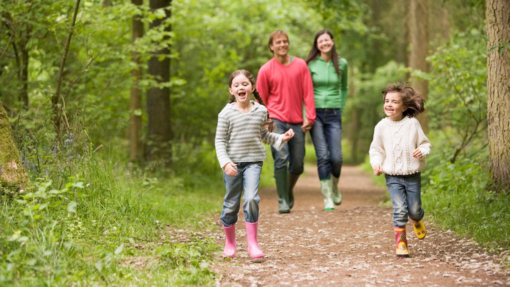 Eltern mit zwei Kindern gehen im Wald spazieren.