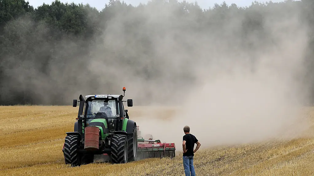 Ein Landwirt fährt mit einer Egge am Traktor über sein Feld und zieht eine Staubwolke hinter sich her. Die anhaltende Trockenheit bereitet den Bauern erhebliche Probleme.