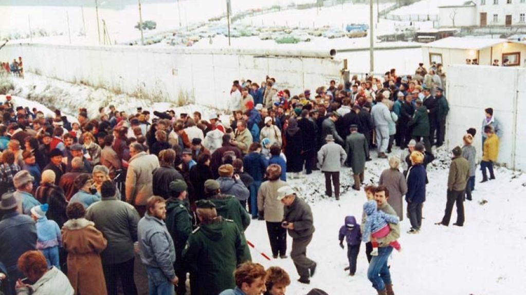 Menschen gehen durch eine Öffnung in der Grenzmauer von Mödlareuth.
