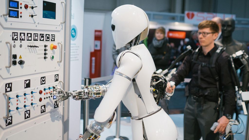 Ein Mitarbeiter des Robotic Innovation Centers steuert bei der CeBIT in Hannover am Stand des deutschen Forschungszentrums für Künstliche Intelligenz mit Hilfe eines Exoskeletts den Roboter AILA.