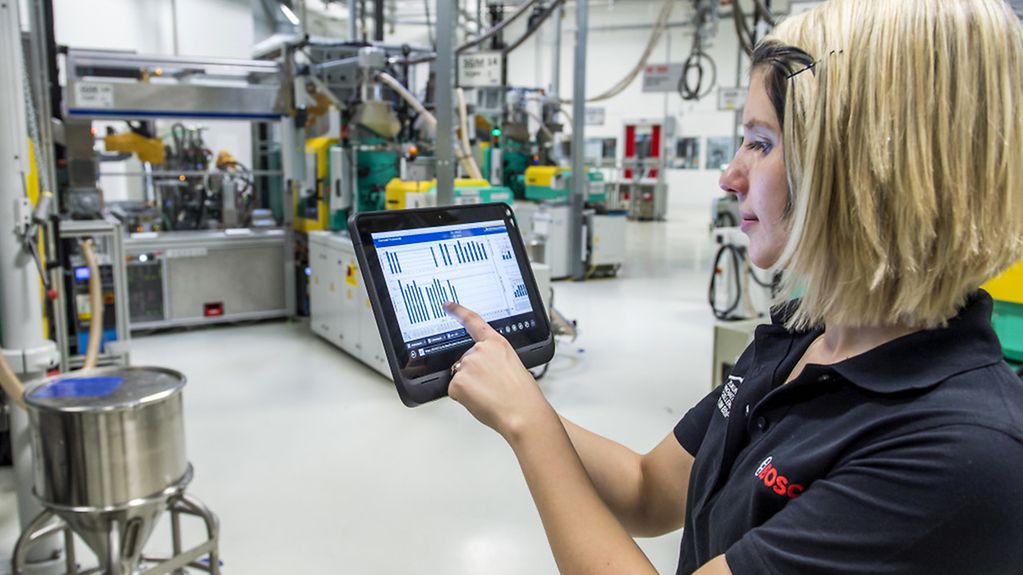 Eine Mitarbeiterin überprüft mit einem Tablet die Betriebsdaten von vernetzten Maschinen für Metallspritzguss.