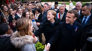 Bundeskanzlerin Angela Merkel und Frankreichs Präsident Emmanuel Macron begrüßen Jugendliche.