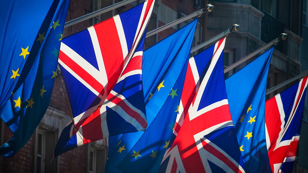 Des drapeaux européens et britanniques alternés flottent ensemble devant la façade d'un bâtiment de brique
