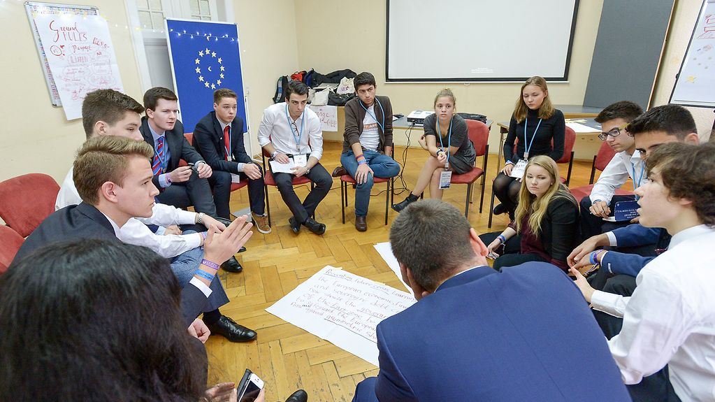 Jugendliche sitzen in einem Gesprächskreis zusammen. Im Hintergrund ist die EU-Fahne zu sehen.