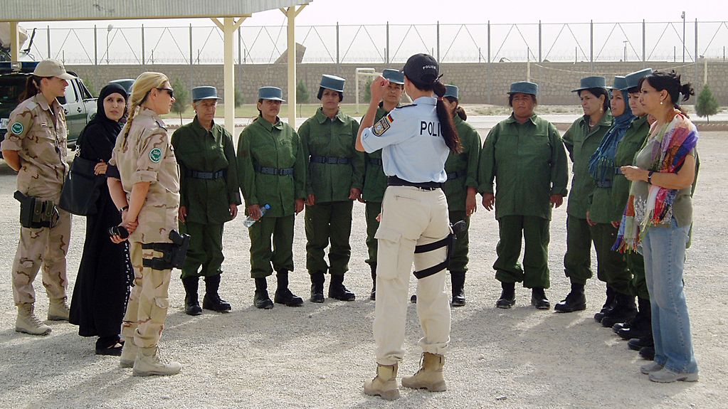 Une policière allemande fait des gestes devant un cercle de forces policières afghanes