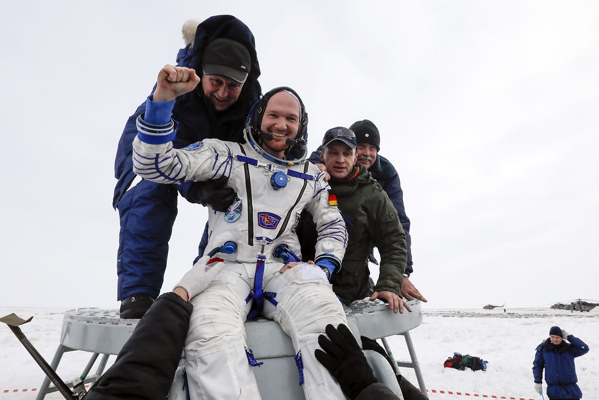 Bodenpersonal hilft ISS-Astronaut Alexander Gerst nach seiner Landung aus der Sojus-Kapsel. Er winkt lächelnd in die Kamera.