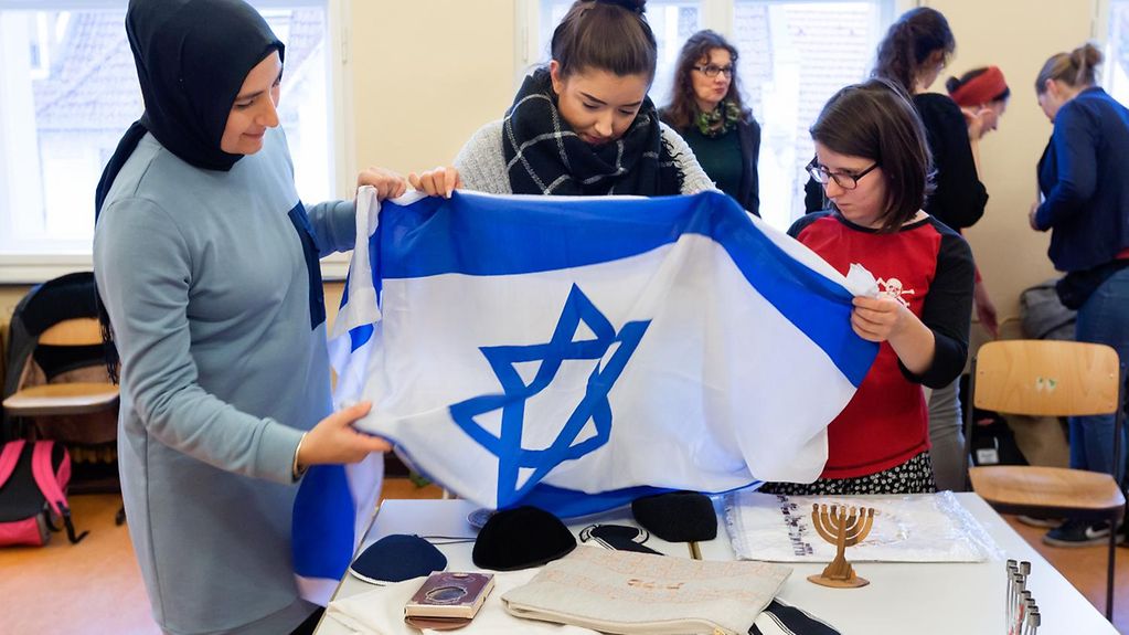 Drei Schülerinnen halten eine Flagge Israels hoch.