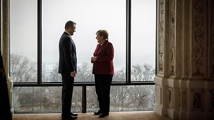Merkel und Pellegrini im Gespräch vor einem Fenster.
