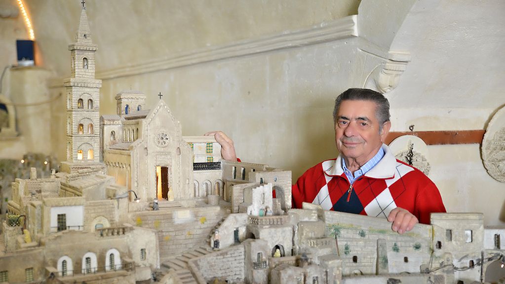 Der Künstler Eustachio Rizzi steht neben einer Nachbildung seiner Heimatstadt Matera. Das Modell zeigt Häuser, Treppen und eine Kirche.