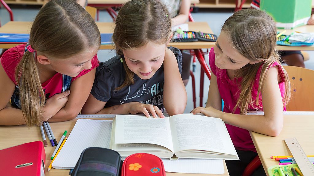 Drei Mädchen lesen in einem Schulbuch.