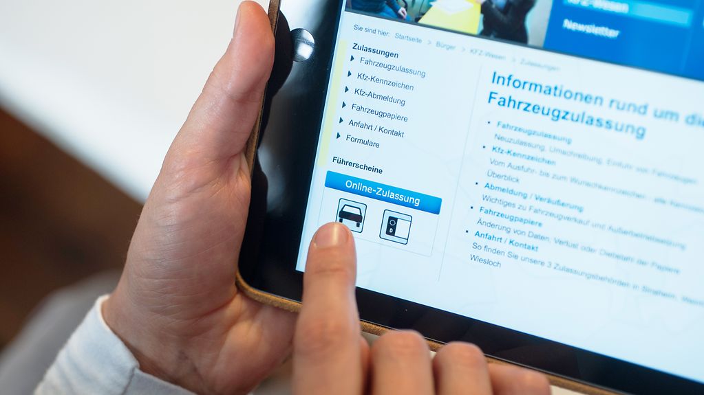 Nahaufnahme eines Tablets in den Händen einer Person. Auf dem Tablet aufgerufen ist die Kfz-Zulassungsstelle des Rhein-Neckar-Kreises, der die Online-Beantragung anbietet.