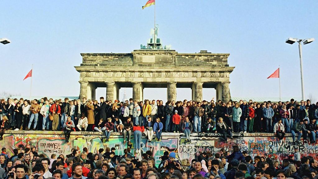 Bewohner aus West- und Ostberlin stehen auf der Mauerkrone am Brandenburger Tor.