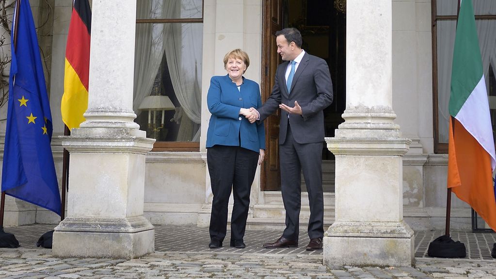 Vor dem irischen Regierungsgebäude stehen Kanzlerin Merkel und ihr irischer AmtsKollege zwischen den Flaggen Deutschlands, Irlands und der Europäischen Union.