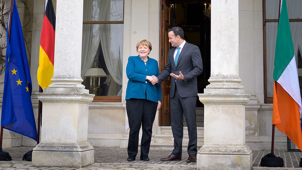 Taoiseach Leo Varadkar greets Chancellor Angela Merkel outside Farmleigh House, framed by the European Union, German and Irish flags.