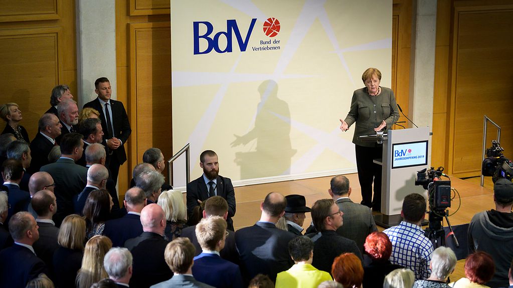 Bundeskanzlerin Angela Merkel spricht beim Jahresempfang des Bundes der Vertriebenen. Hinter ihreine große weiße Leinwand mit dem BdV-Logo, vor ihr zu sehen ist das Publikum.