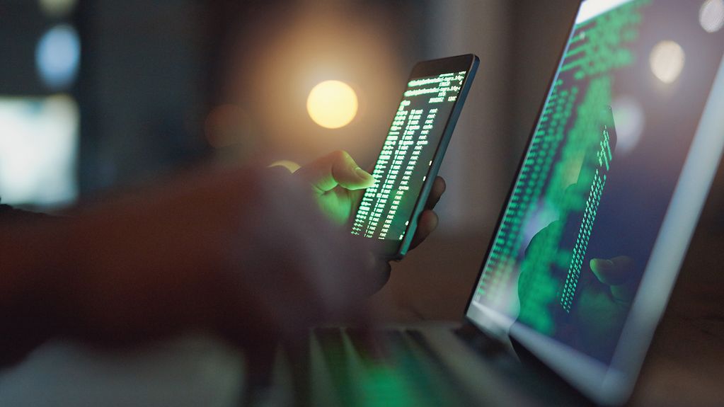 Ein Hacker nutzt ein Smartphone und einen Computer im Dunkeln.