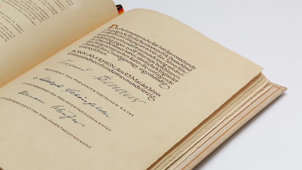 Seite aus dem Grundgesetz mit der Unterschrift von Konrad Adenauer als damaliger Präsident des Parlamentarischen Rats sowie den Unterschriften des 1. und 2. Vizepräsidenten Adolph Schönfelder und Hermann Schäfer. 