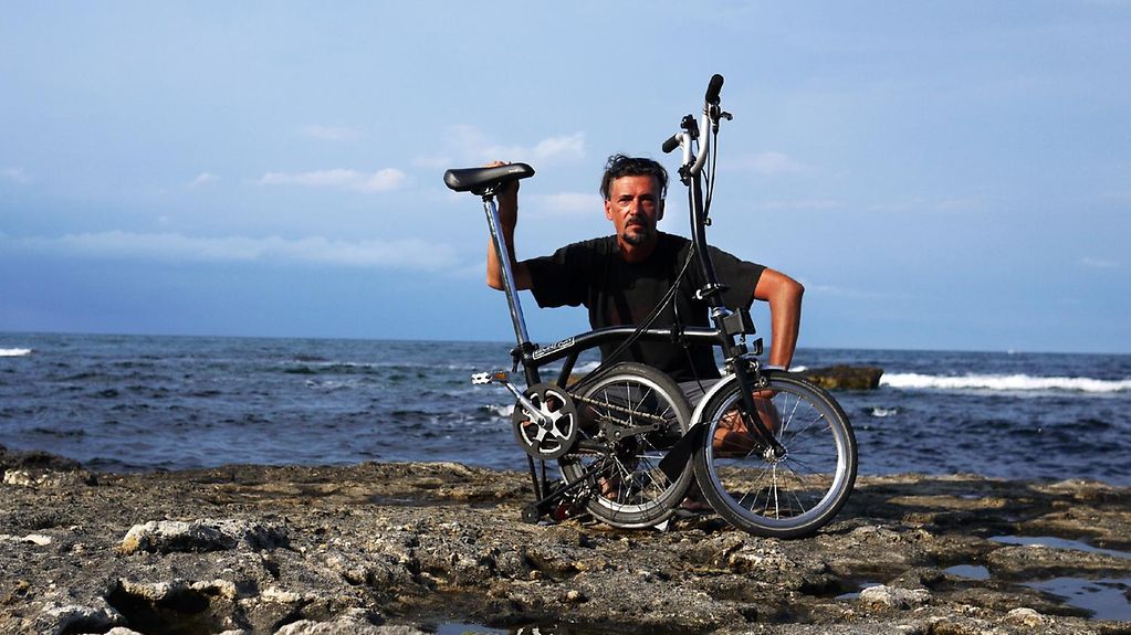 Mario Lang hockt auf einem Felsvorsprung im Meer, vor ihm sein Faltrad.