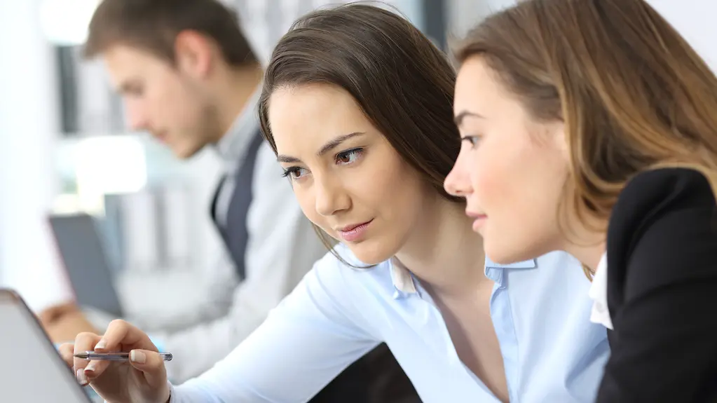 Zwei Frauen arbeiten zusammen mit einem Laptop im Büro.